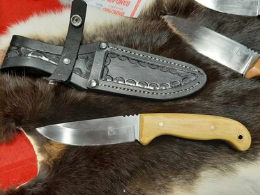 A custom knife with a light brown handle shown on a piece of fur with its black leather sheath.