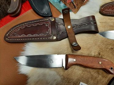 A custom knife with a brown handle shown on a piece of fur with its intricately designed brown leather sheath.