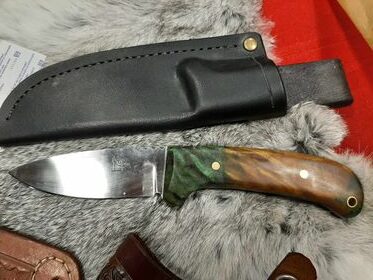 A custom knife with a green & brown handle, shown on a piece of fur with its black leather sheath.