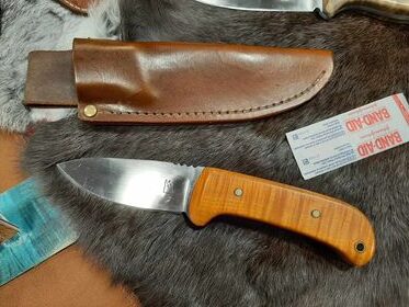 A knife with a light brown handle, laid on a piece of fur with its brown leather sheath.