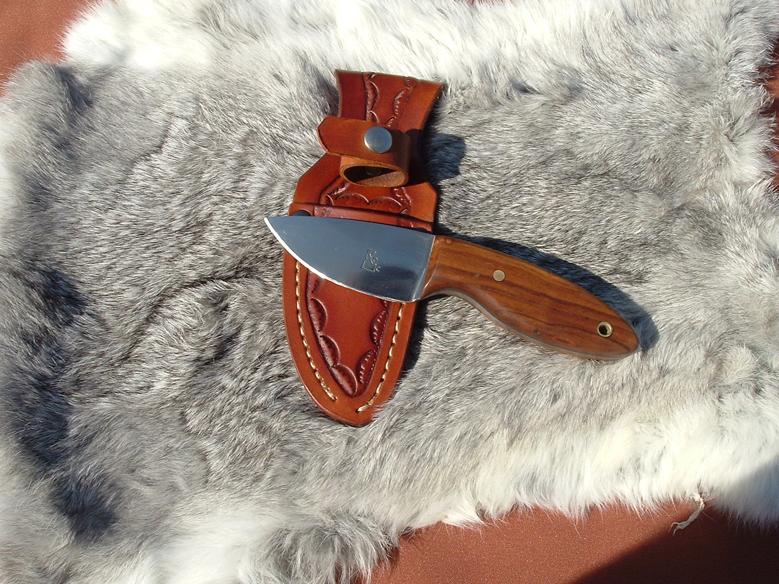 A small knife laying on a brown leather sheath, with a gray fur backdrop